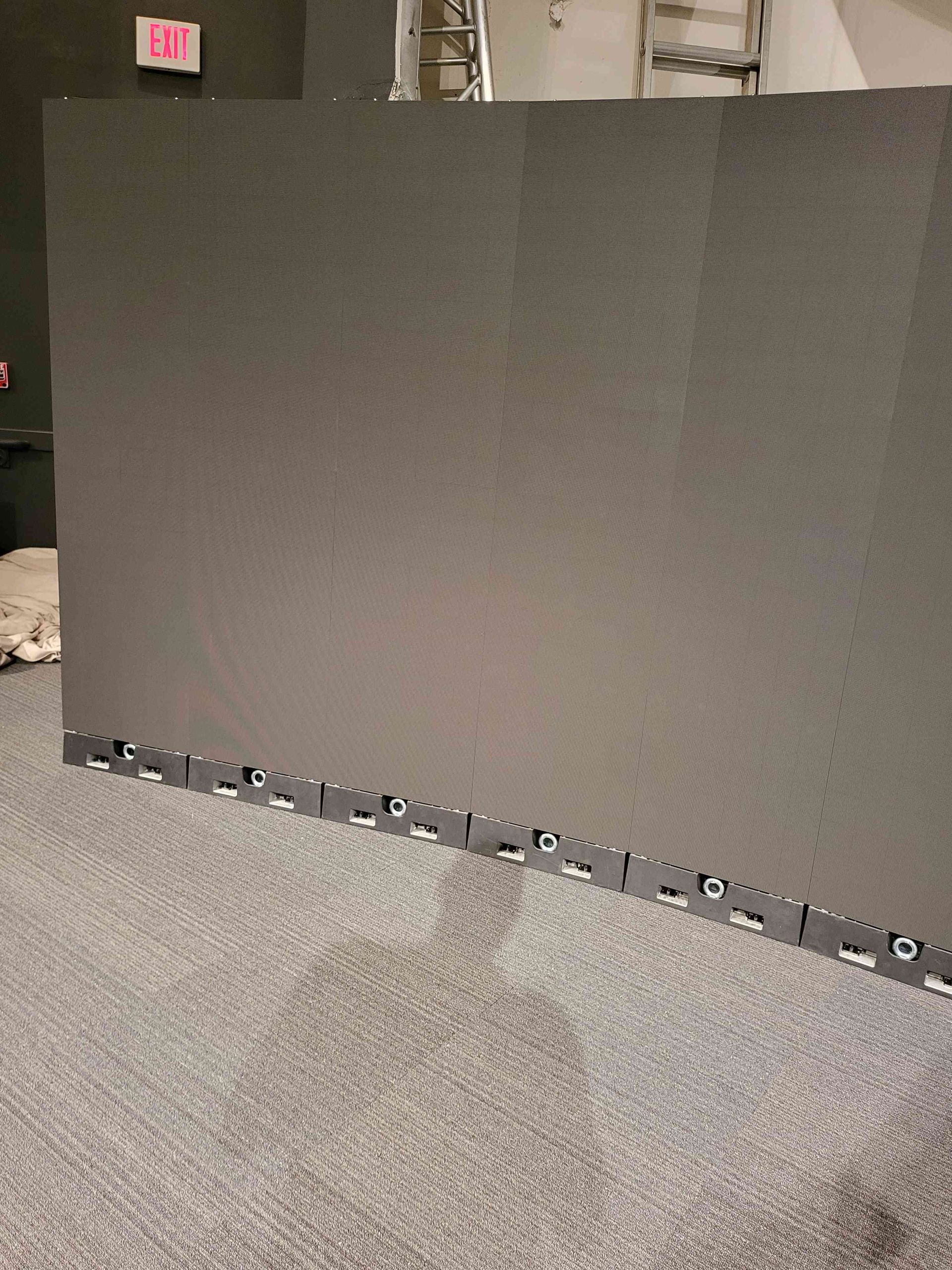 Large gray LED video wall on a gray carpet in a room, a red exit sign is visible.