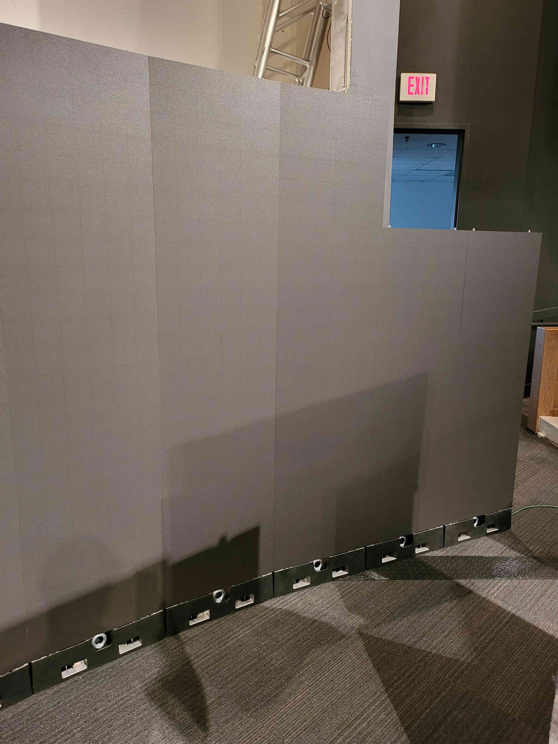 Dark gray modular wall with black edging, set on gray carpet. Exit sign in background.