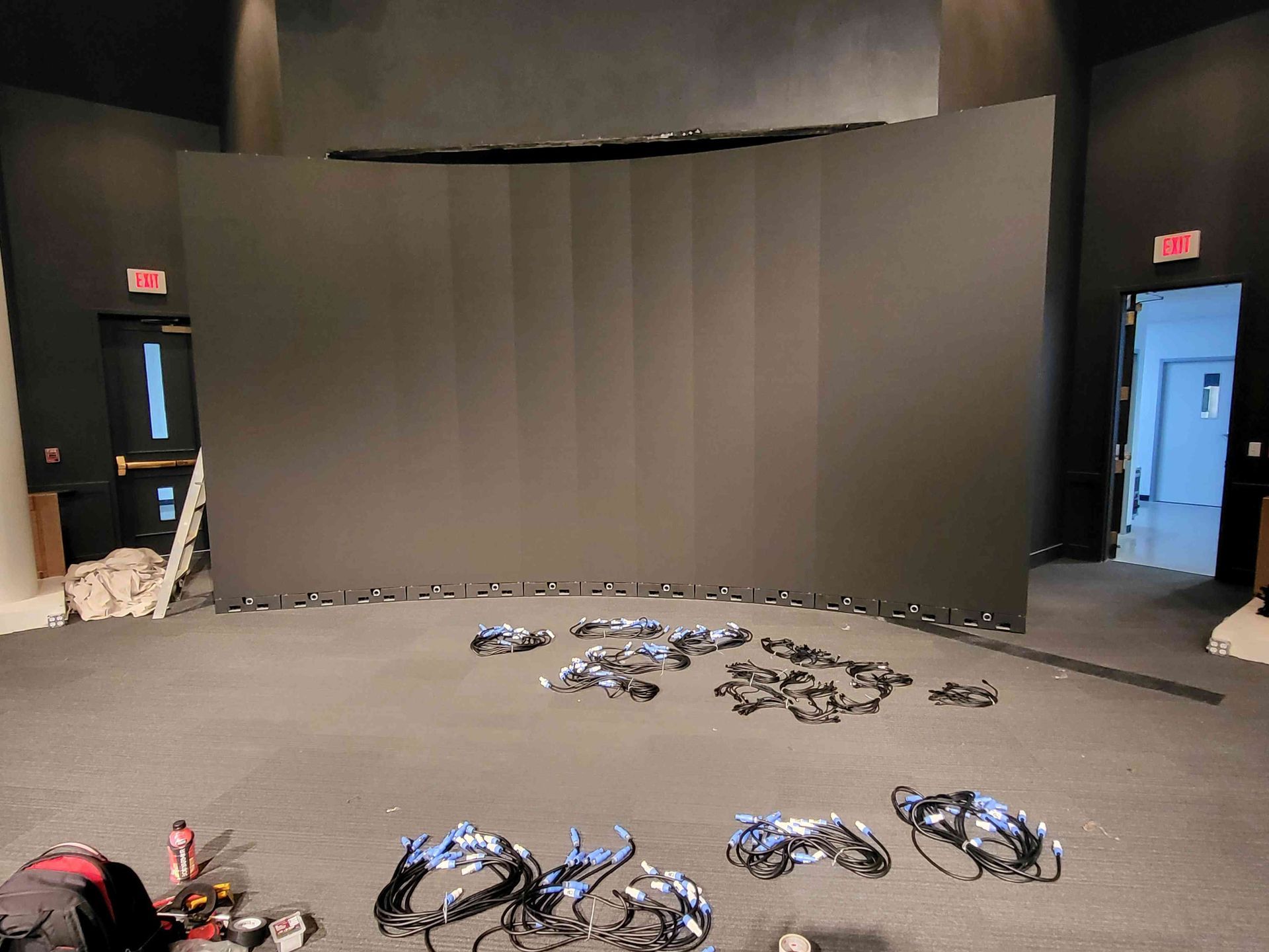 A large, curved black screen dominates an empty room, surrounded by cables and equipment on the floor.