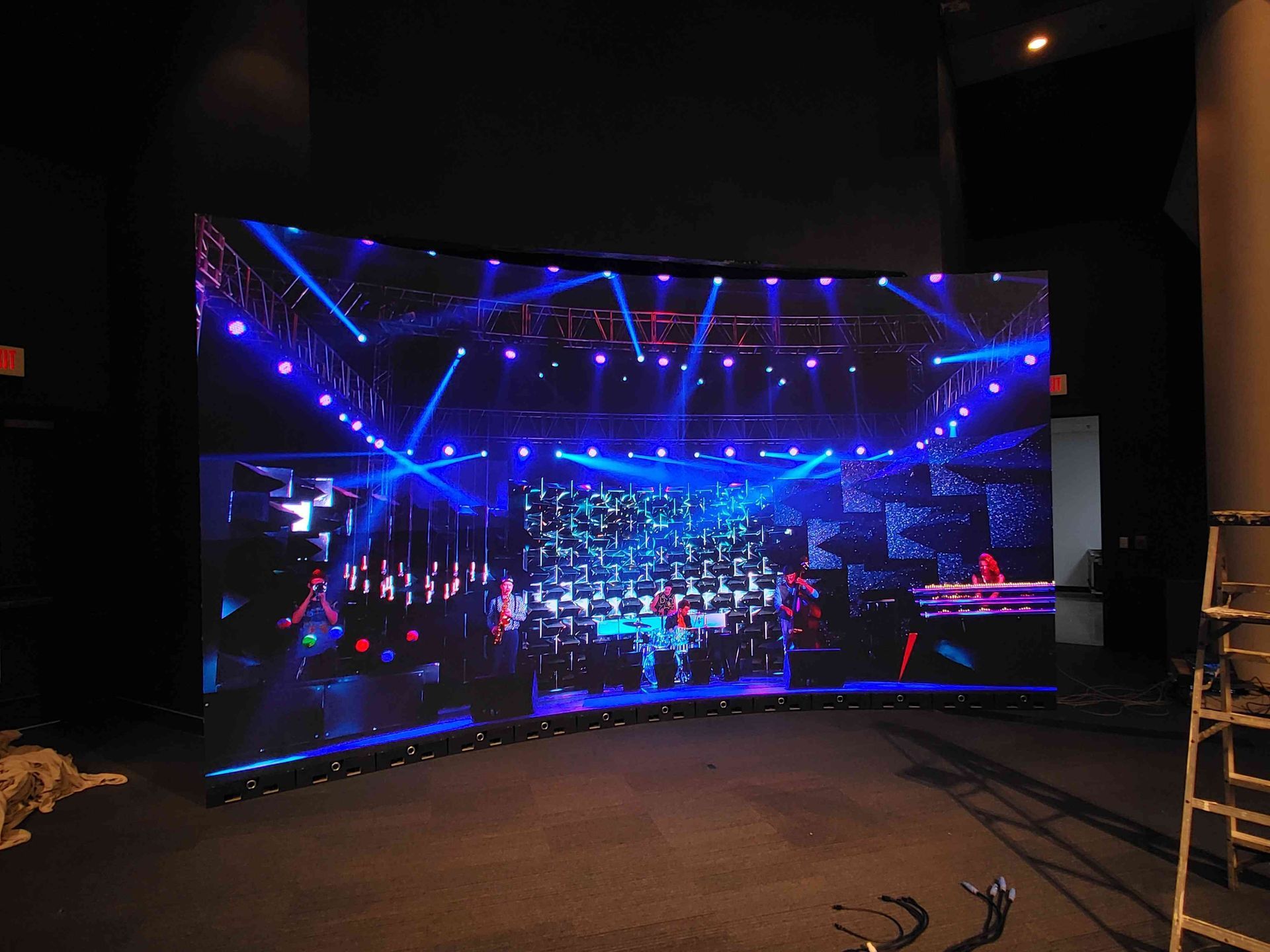 Curved LED screen displaying a blue stage with performers and lights in a dark room.