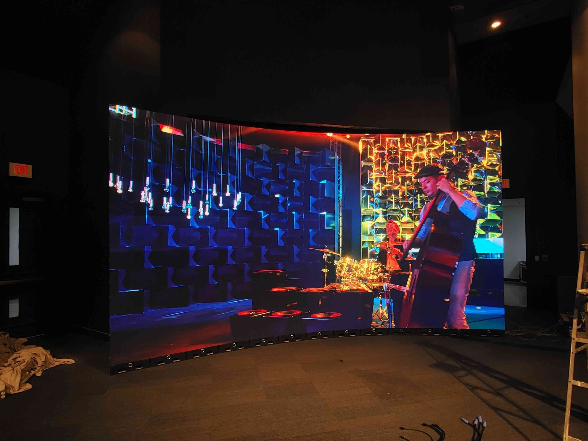A curved LED screen displays a musician playing, illuminated in blue and gold, set in a dark room.
