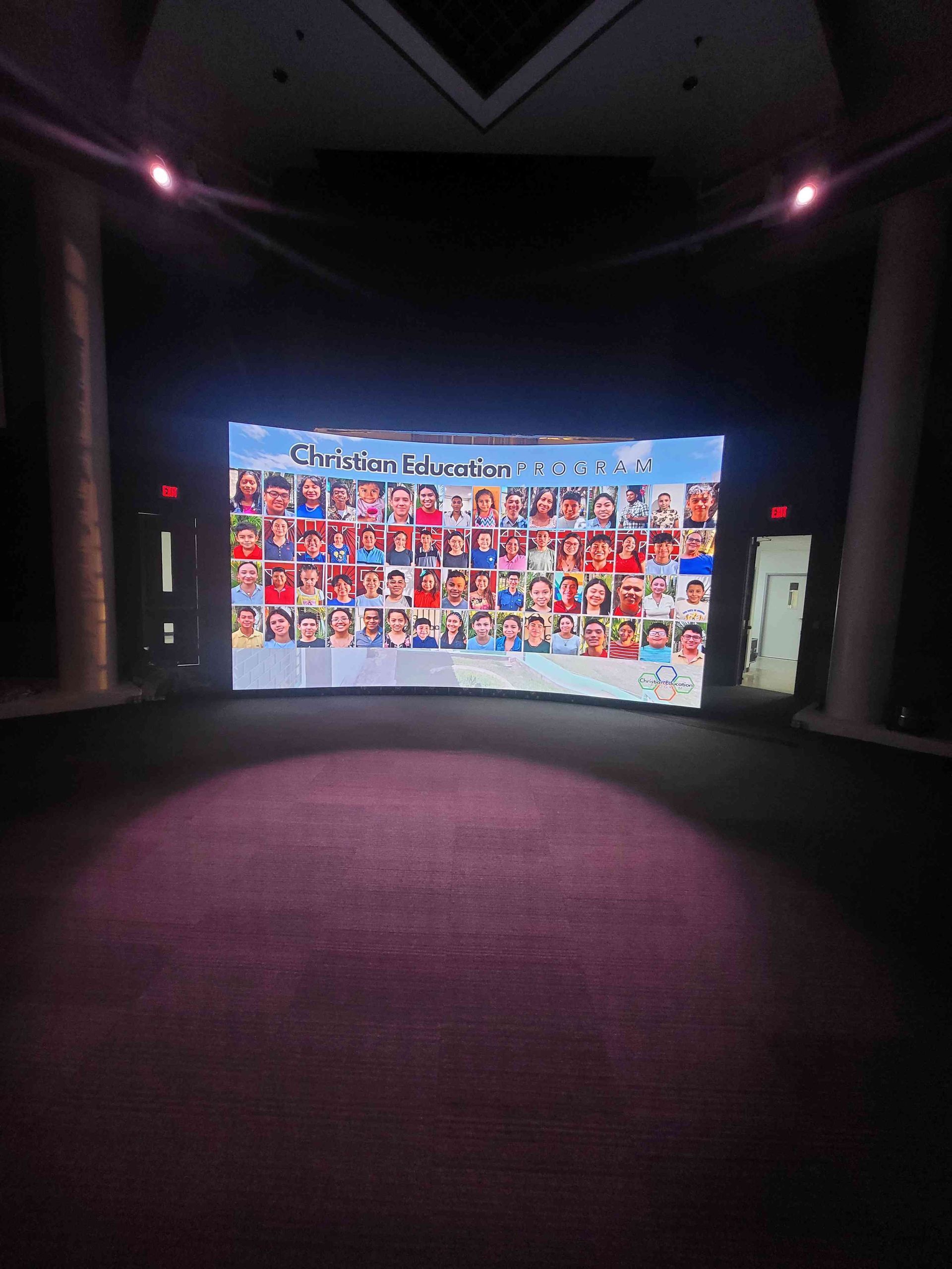 A large screen displays numerous photos of people in a dim, formal setting.