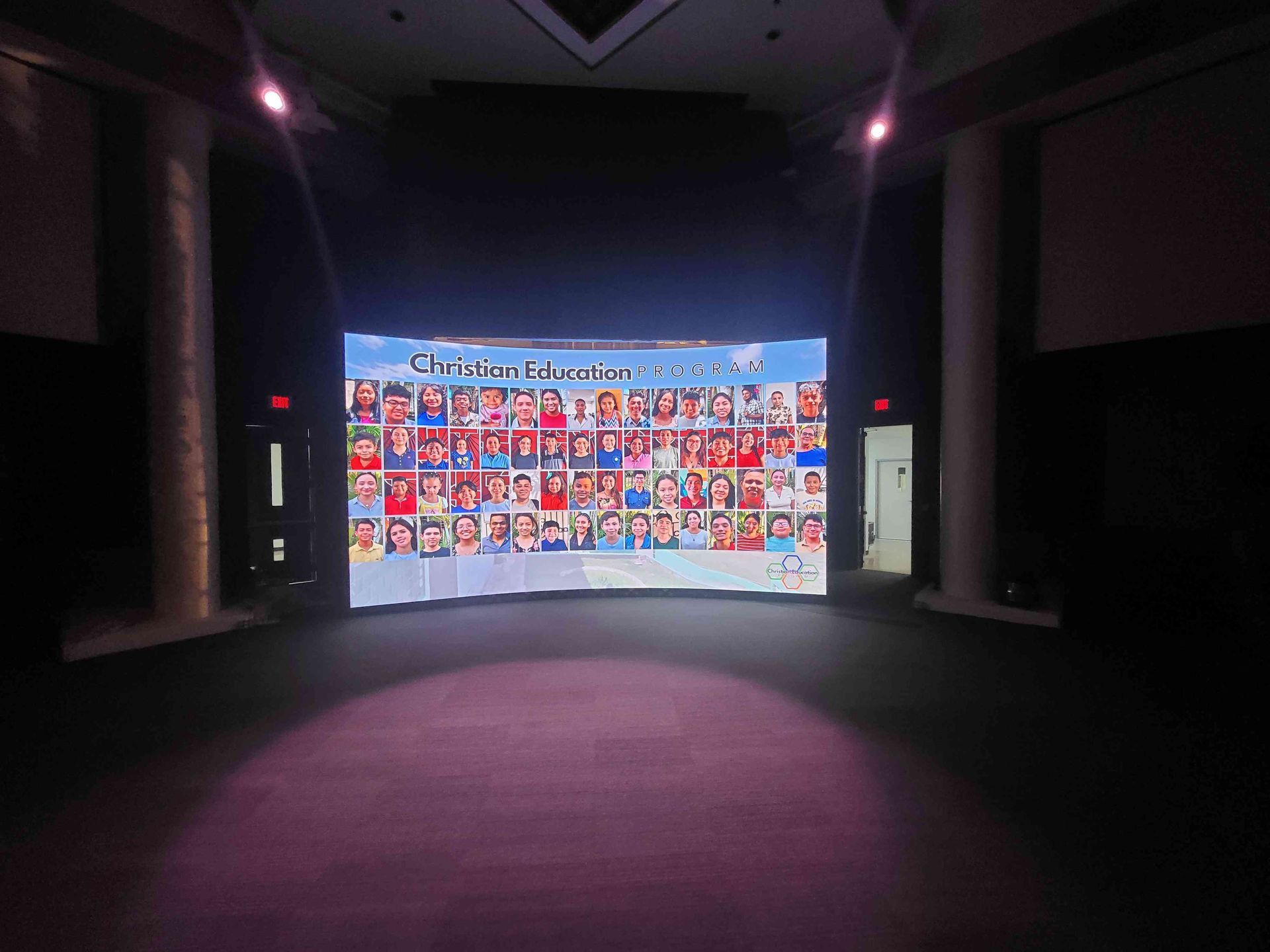 Curved screen displaying many children's photos; stage setting with columns and dark background.