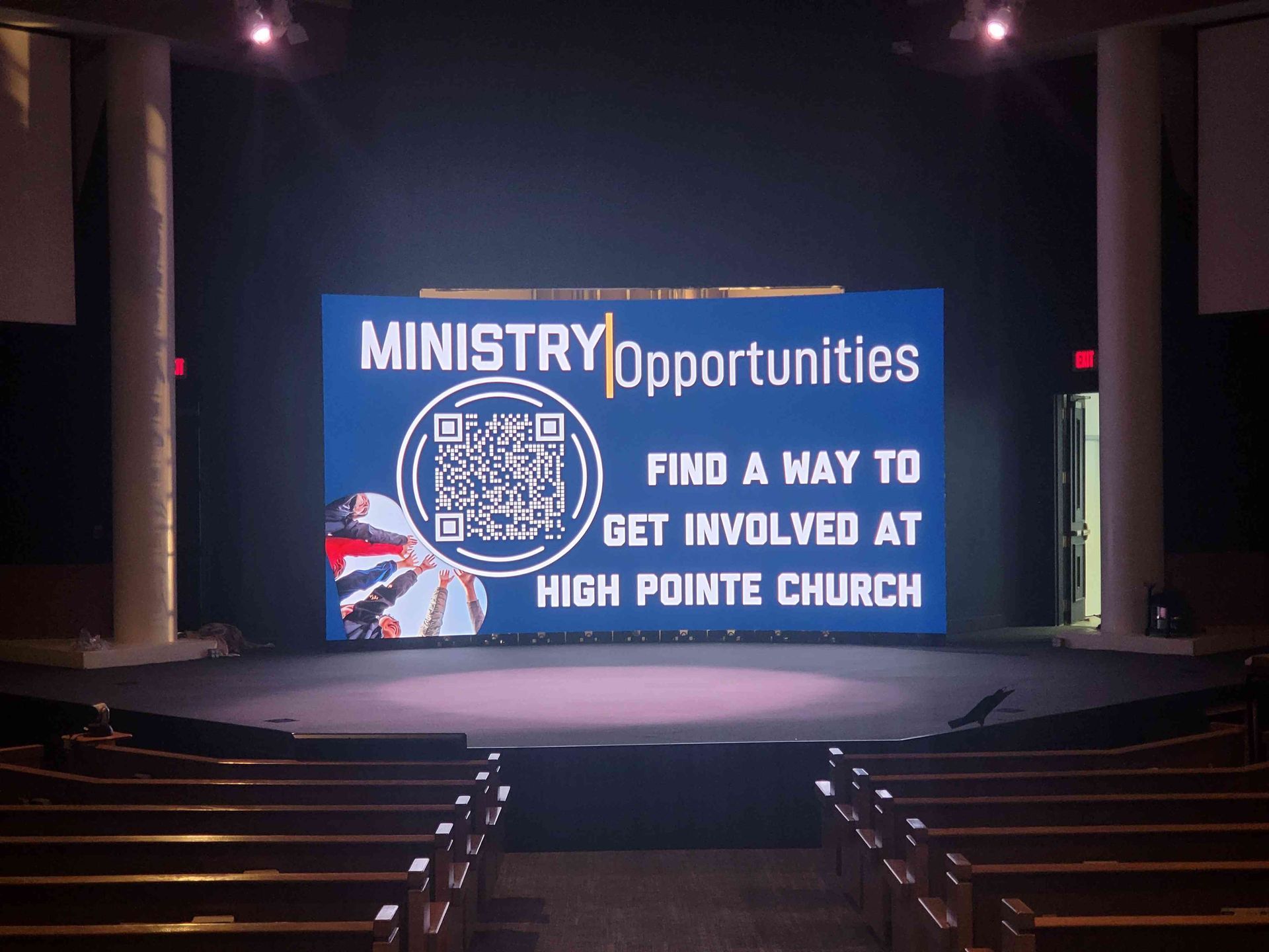 Digital sign in a church auditorium promoting ministry opportunities at High Pointe Church. Contains a QR code and text on a blue background.