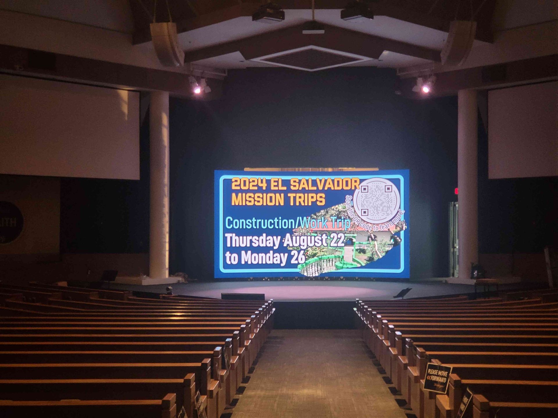 Church interior with stage and screen advertising 2024 El Salvador mission trips. Text on screen with a map.