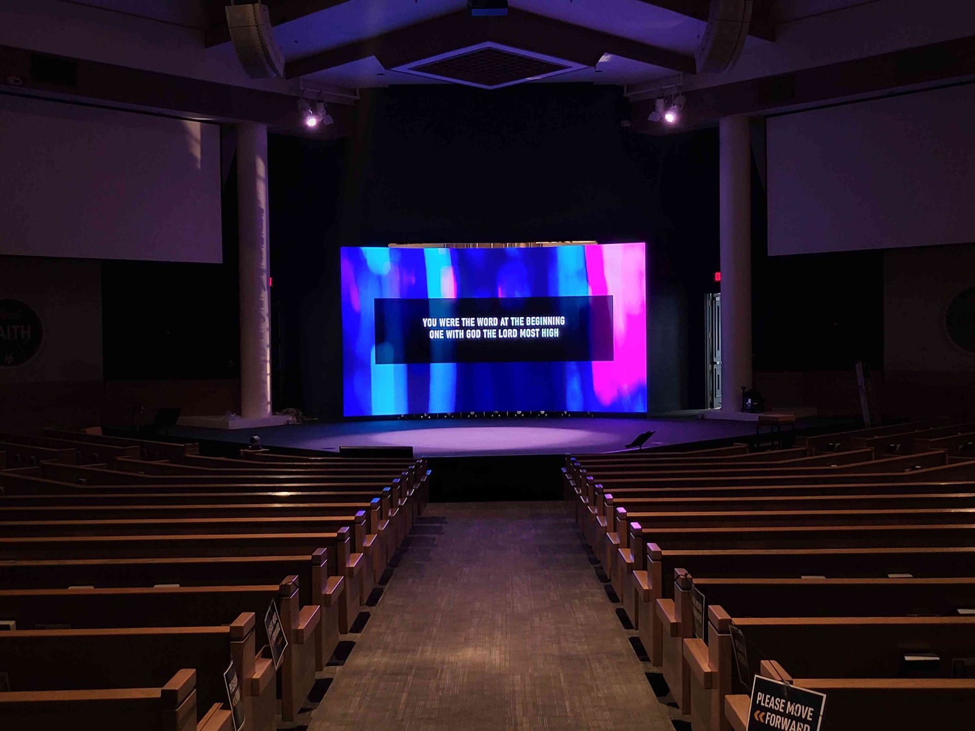 An empty church sanctuary with a stage and large screen displaying text over an abstract background.
