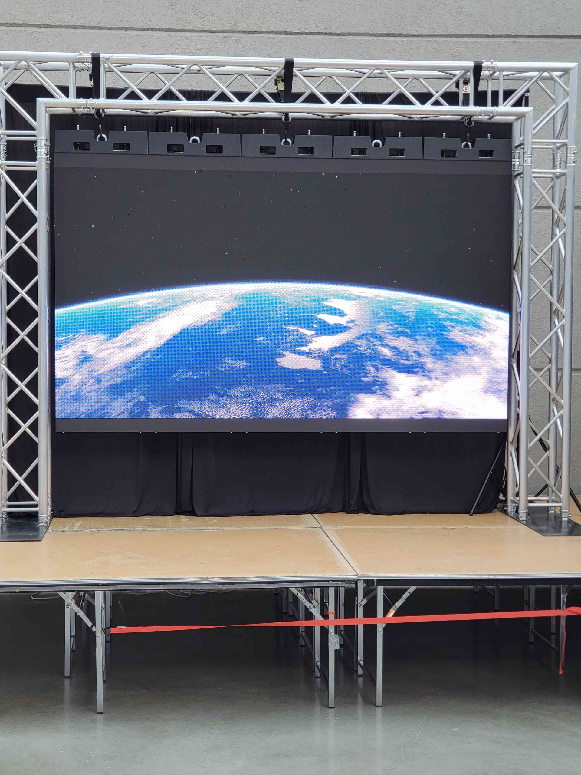 LED screen displaying Earth in space, mounted on a truss system and stage.