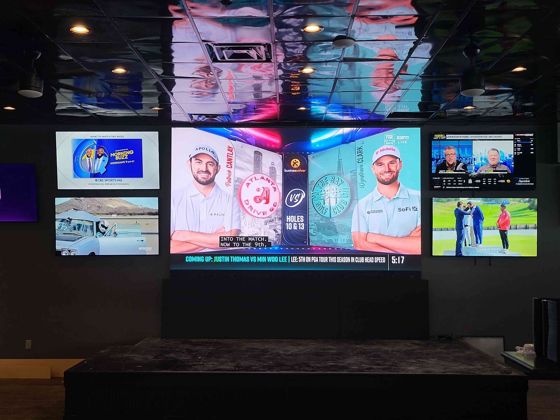 A wall of TVs displays golf events and programming in a sports bar setting.