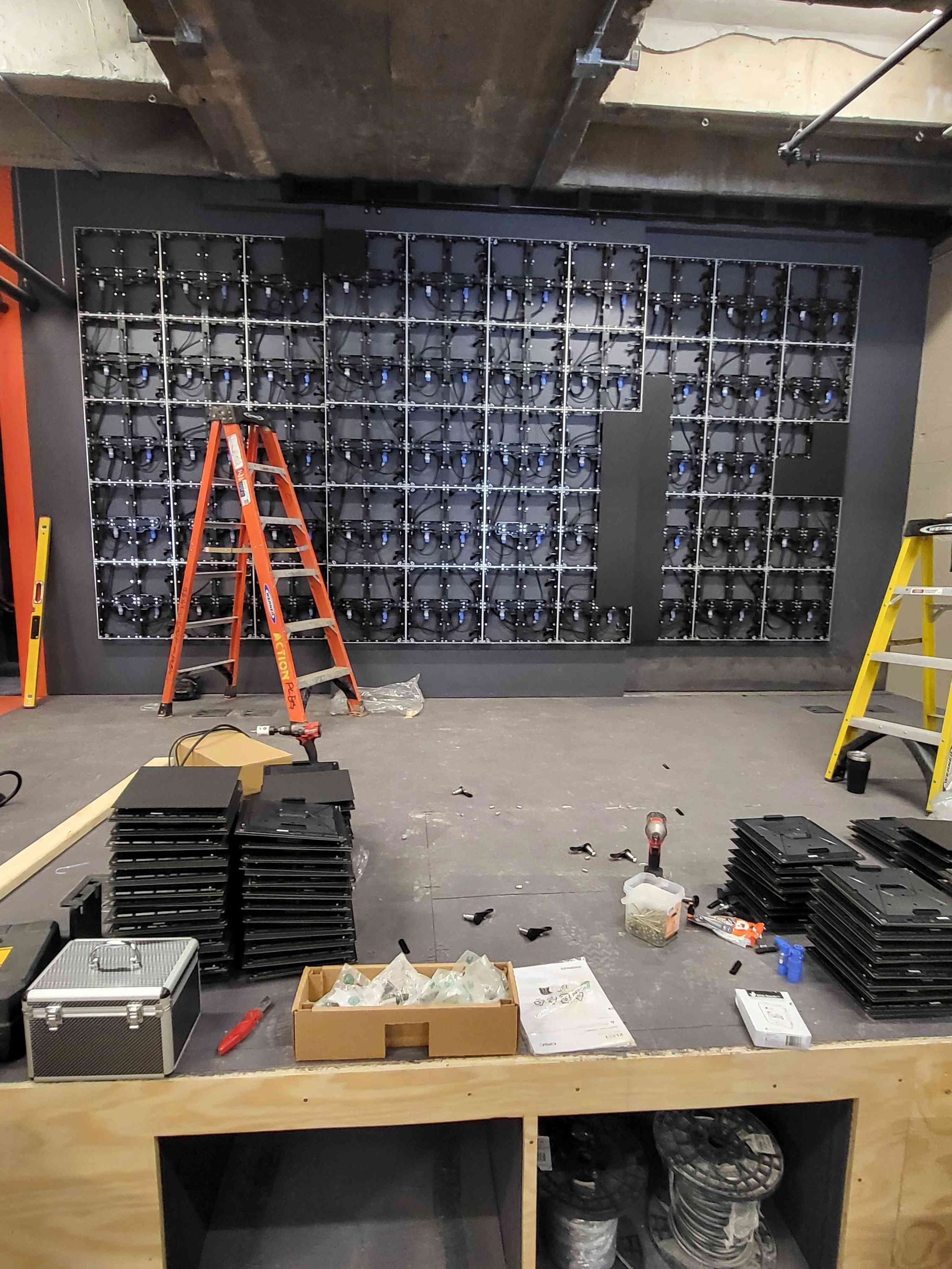 Wall with installed screens in progress, ladders, tools, and materials scattered in a work area.