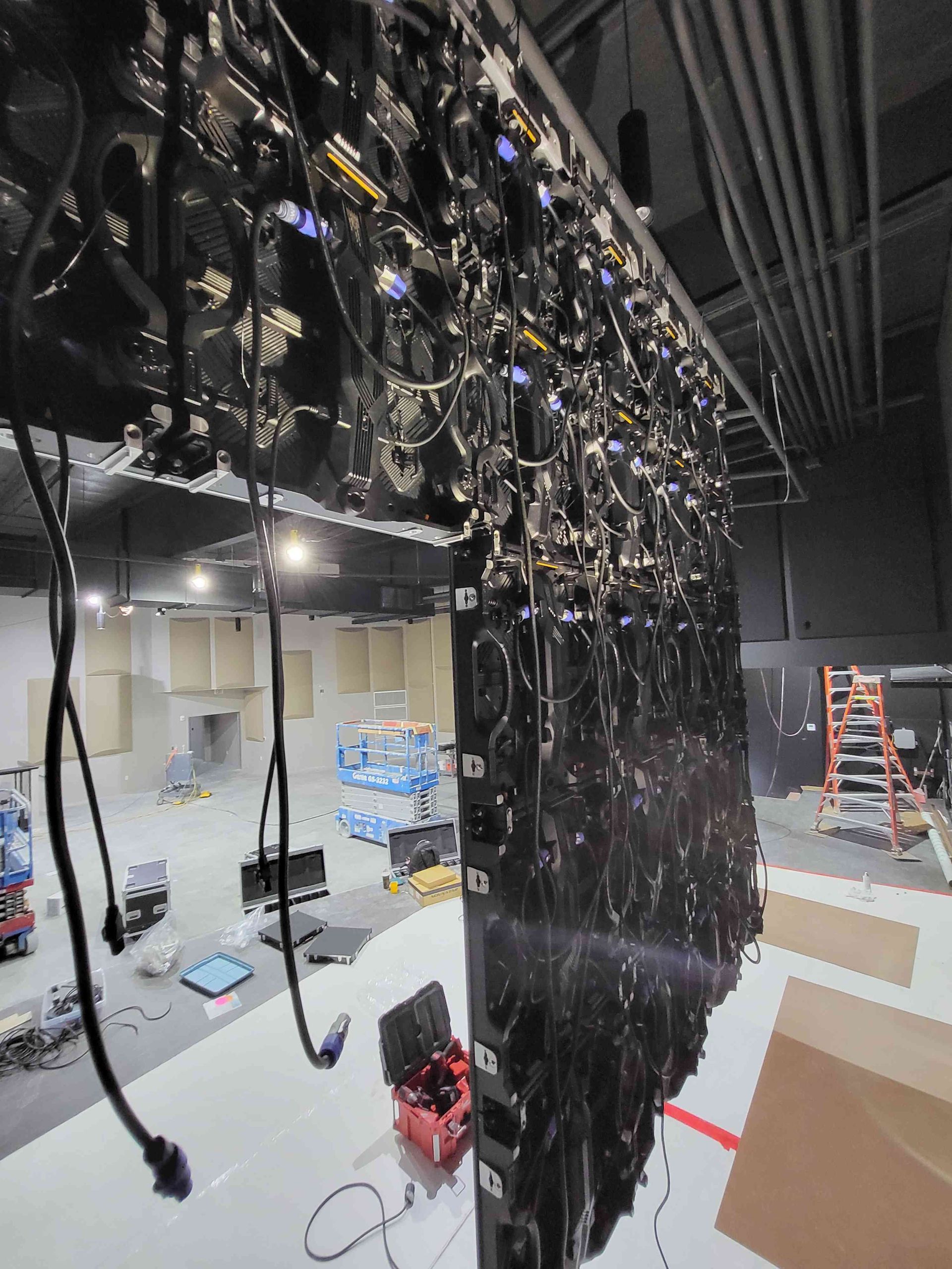 Overhead view of a theater's stage setup with black lighting equipment, cables, and a partially visible stage.