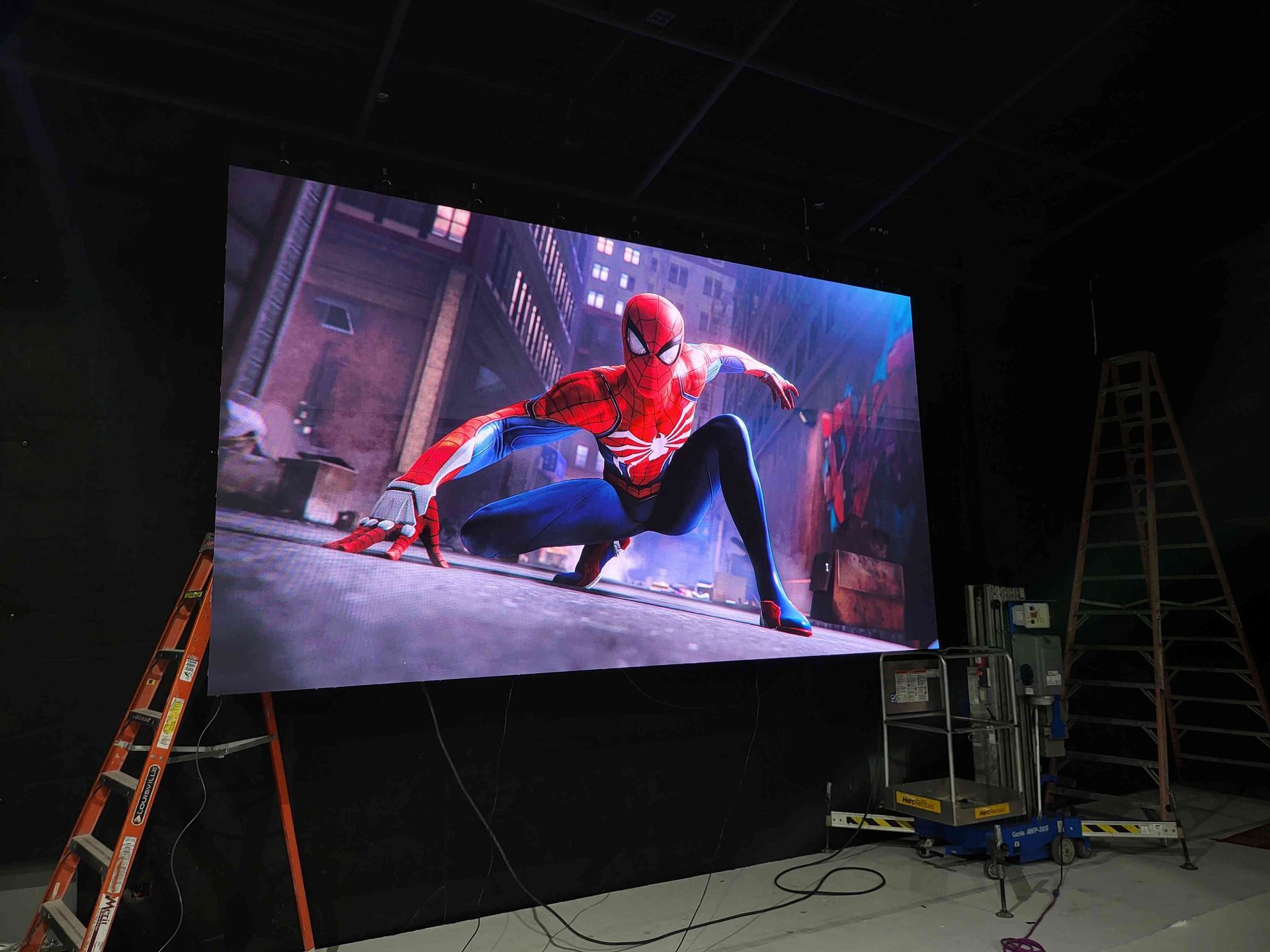 Spider-Man displayed on a large screen in a studio. A ladder and equipment are in the background.