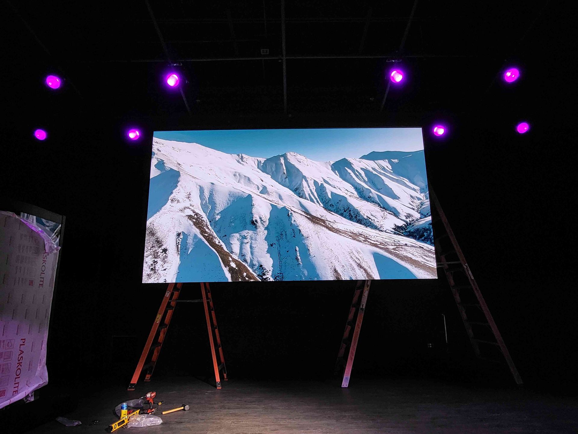 Snowy mountain landscape displayed on a large screen, set up on a stage with purple stage lights.