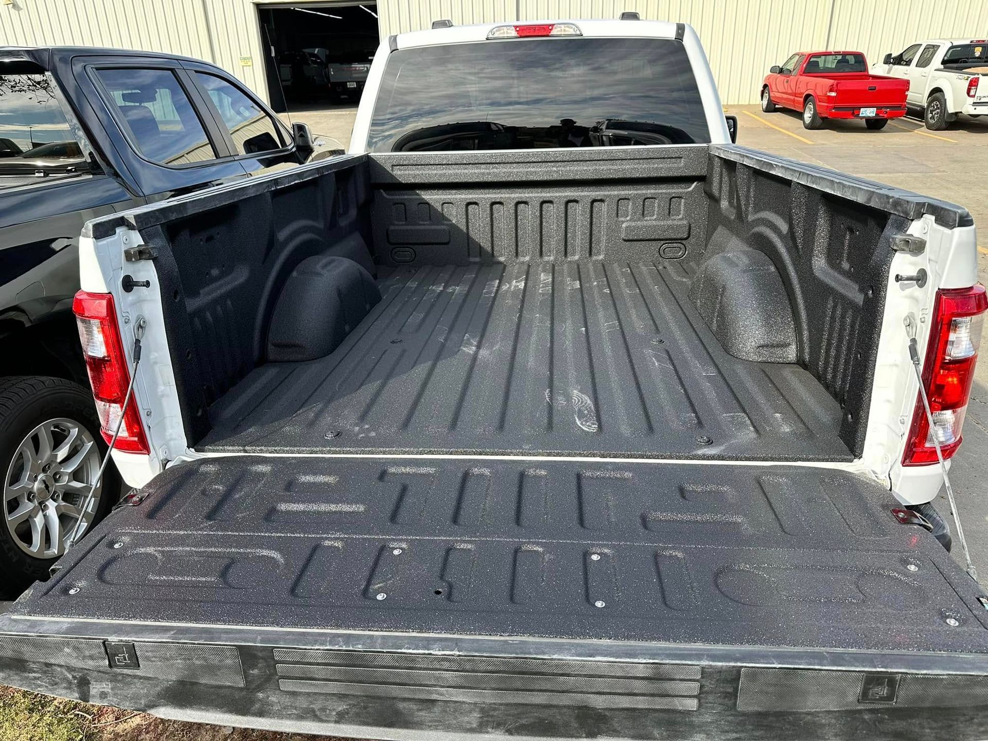 White pickup truck bed, open, revealing a black textured bed liner, parked outside.