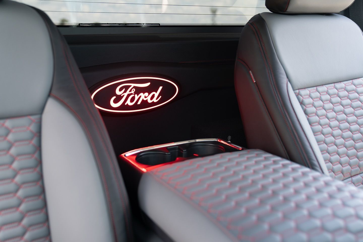 Close-up of a truck's interior featuring a glowing red Ford logo, cupholders, and patterned gray seats.