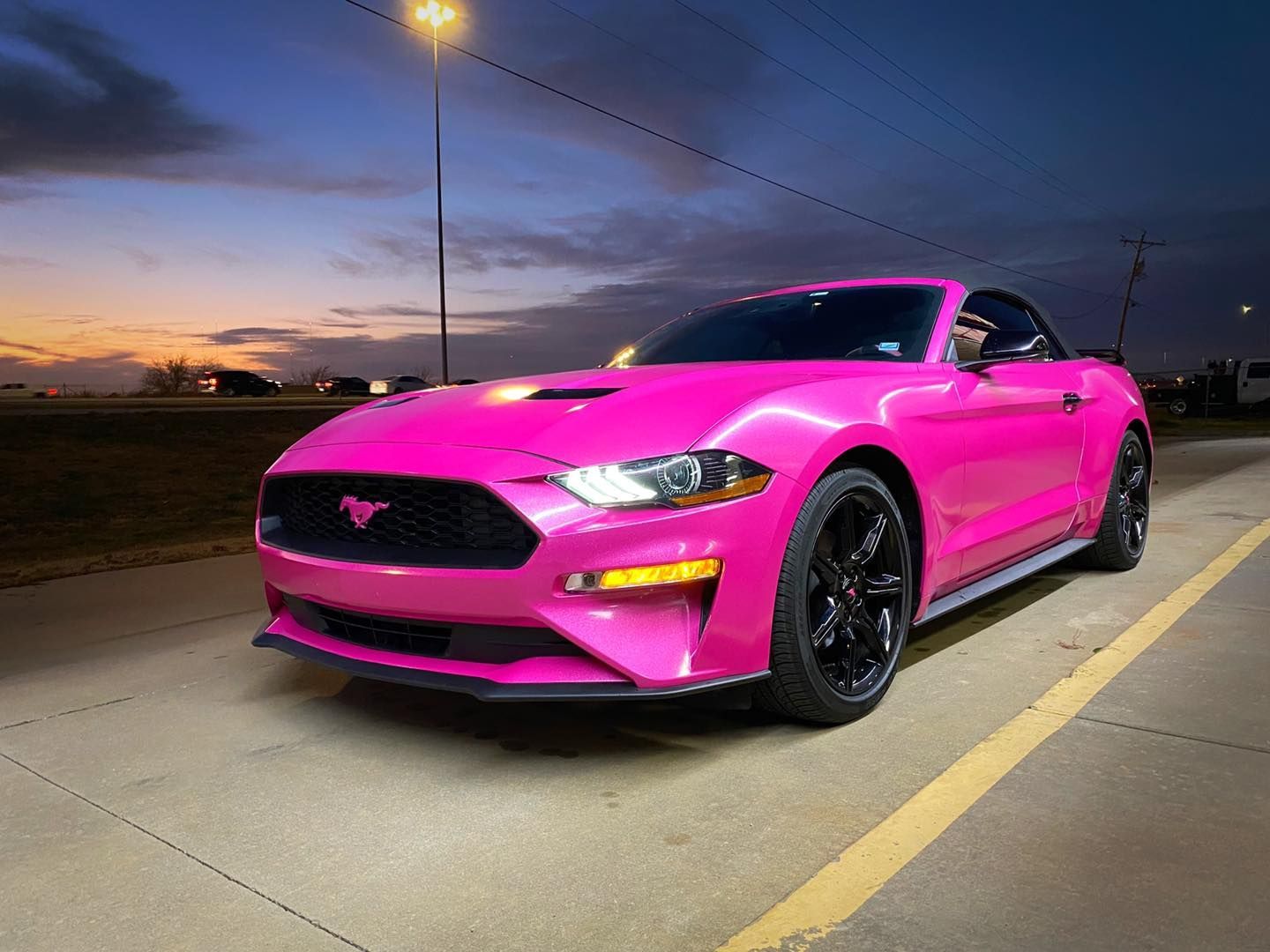 Bright pink Ford Mustang, black wheels, parked outdoors at dusk.