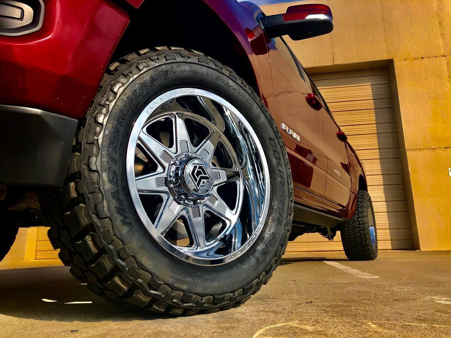 Red truck with chrome wheels parked near a building.