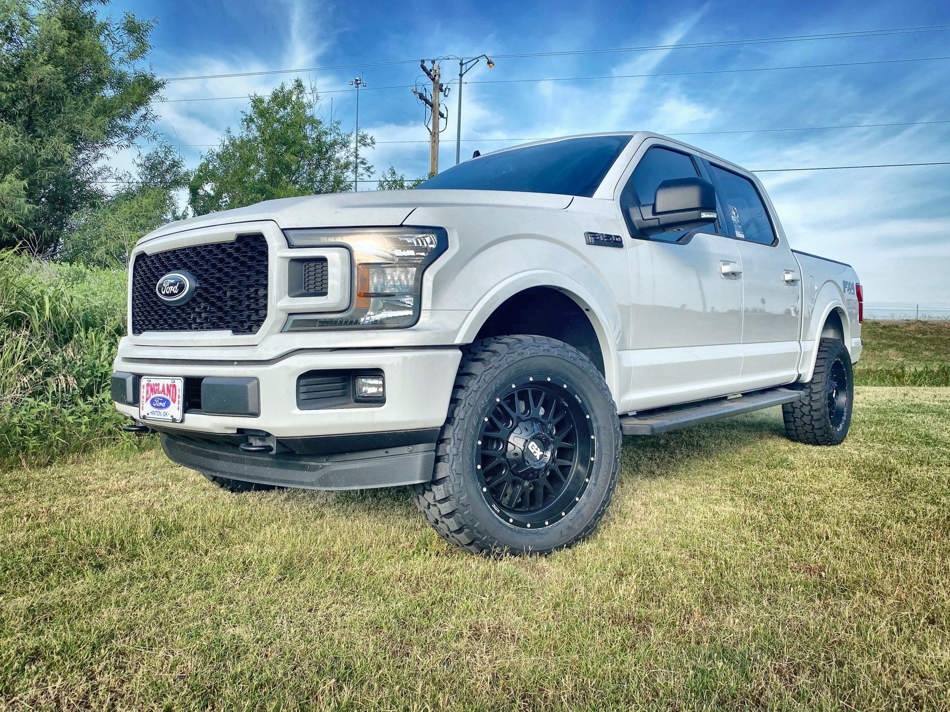 White Ford truck with black wheels on green grass under a blue sky.