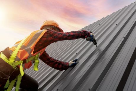 A man is working on a metal roof with a drill.