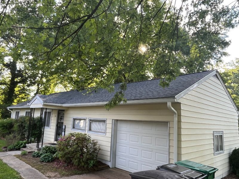 A small white house with a garage and a roof surrounded by trees.