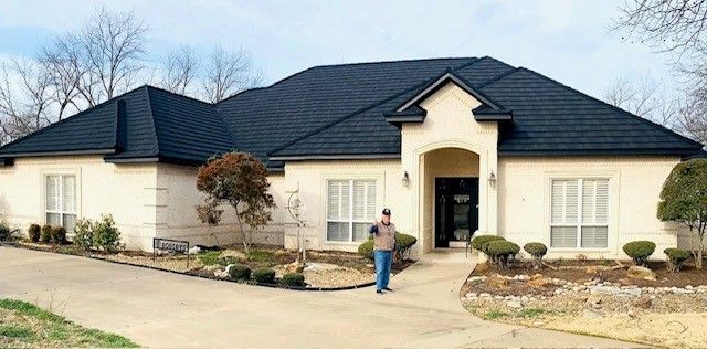 A man is standing in front of a large white house with a black roof.