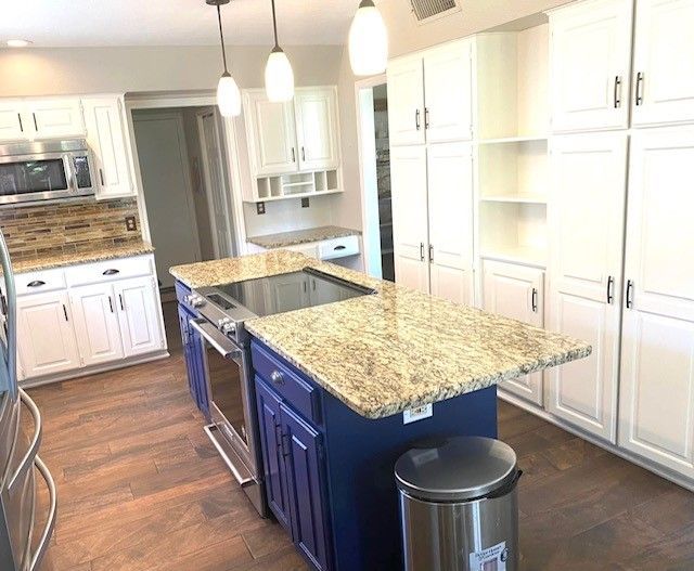 A kitchen with a blue island , white cabinets , granite counter tops and stainless steel appliances.
