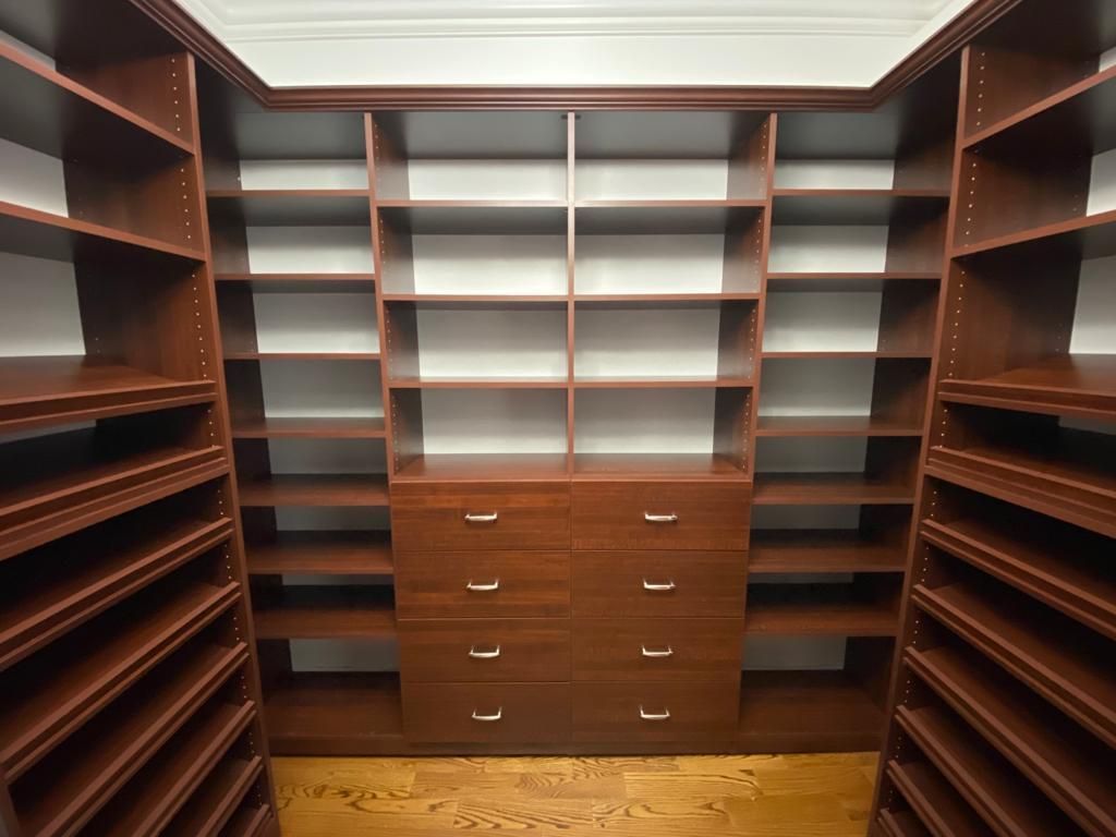 Empty, custom-built walk-in closet with multiple shelves and drawers made of dark wood.