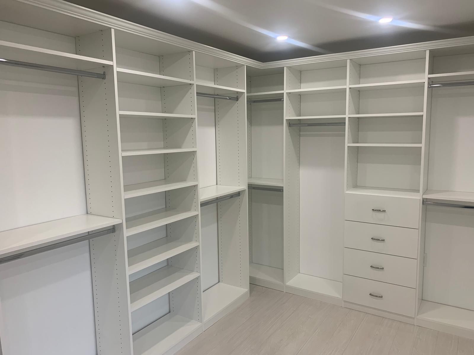 White walk-in closet with shelves, drawers, and hanging rods. Empty, well-lit interior.