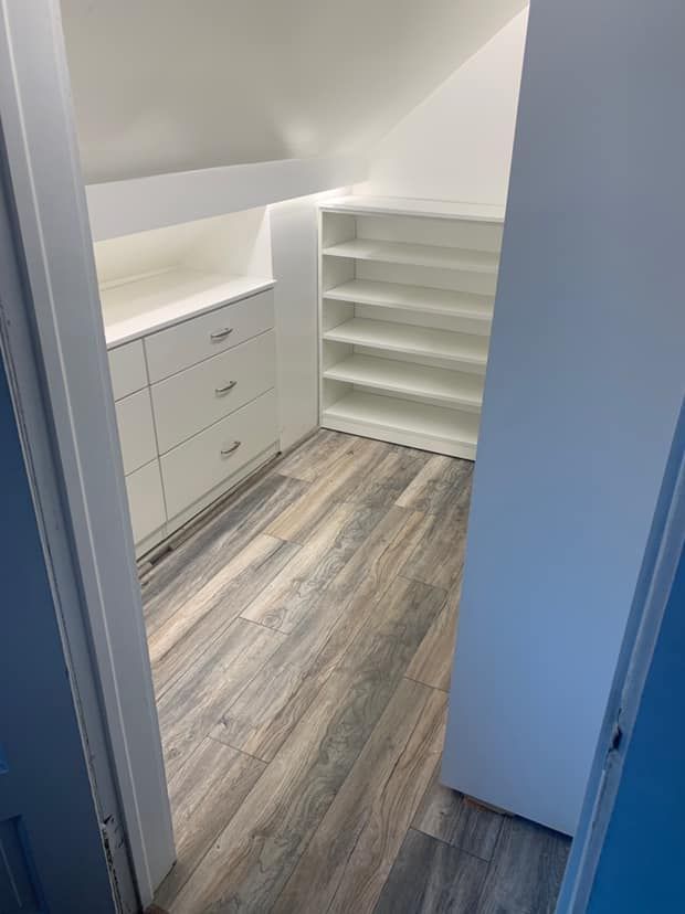 Walk-in closet with white shelves and drawers, wooden-look flooring, and angled ceiling.