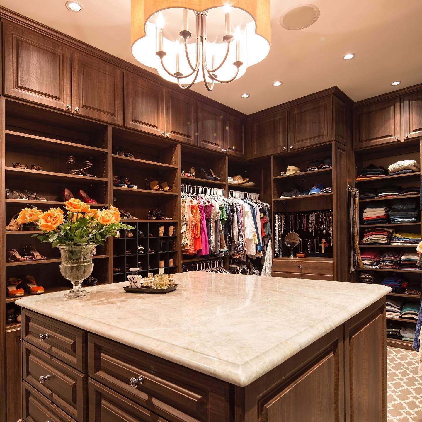Luxurious walk-in closet with dark wood shelves filled with shoes, clothes, and accessories, and a center island with a marble countertop.