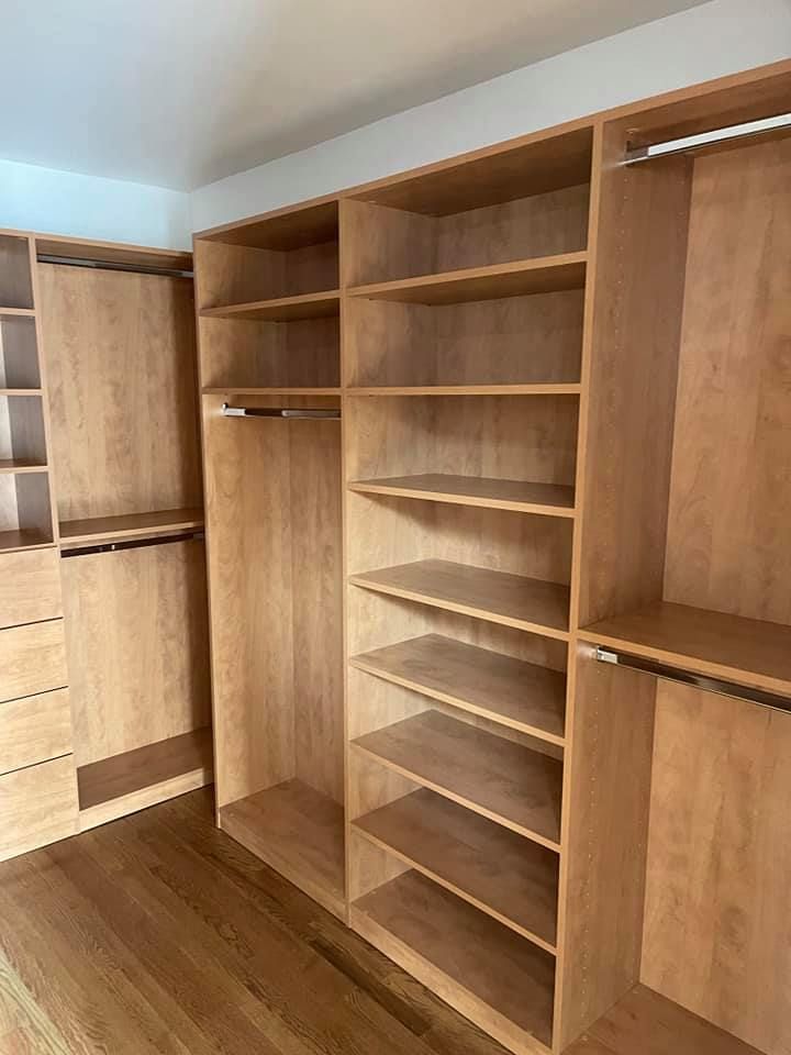 Empty, light-wood closet with shelves and hanging rods, built-in to a room with wood flooring.