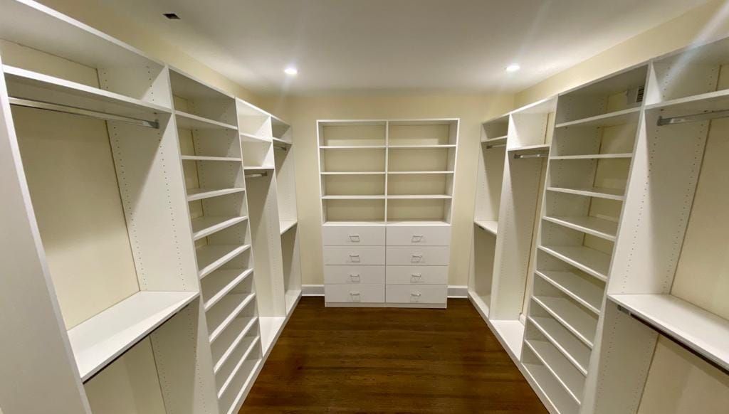 White custom closet with shelves, drawers, and hanging rods. Brown wood floor.