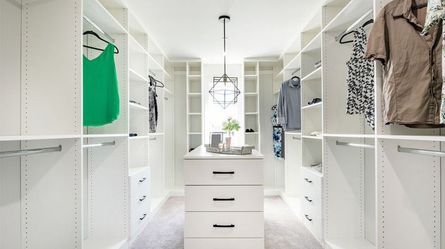 White walk-in closet with central island. Clothes hang on racks; drawers and shelves line the walls.