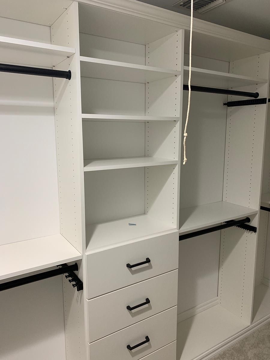 White closet organizer with shelves, drawers, and hanging rods.