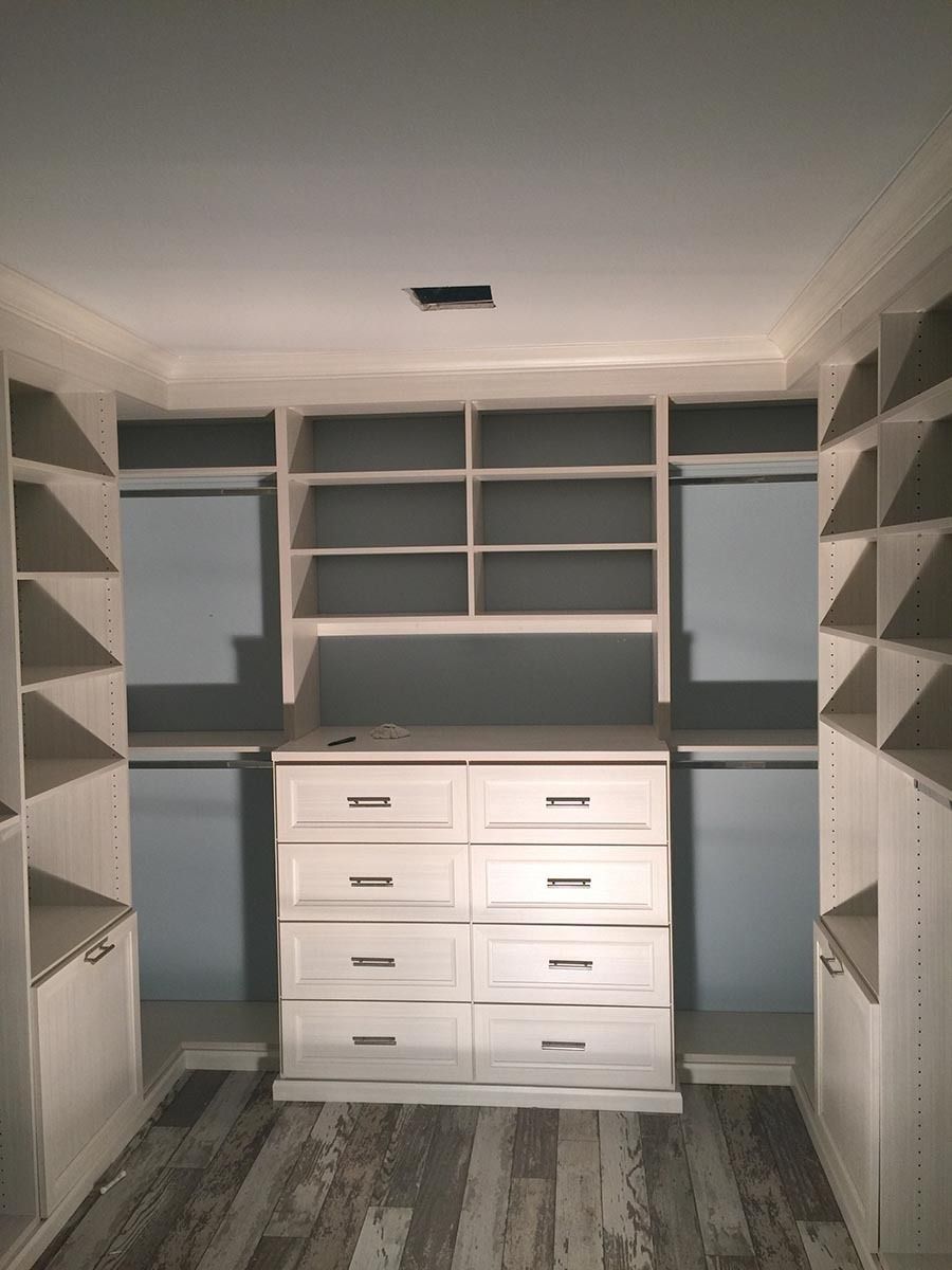 Walk-in closet with white cabinets, shelves, and a dresser. Gray walls and flooring.