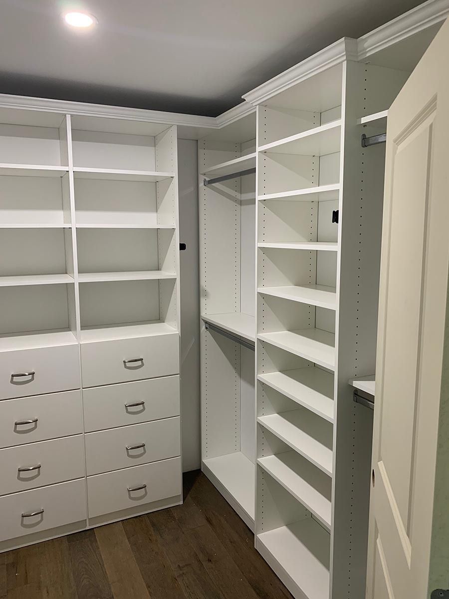 White walk-in closet with shelves, drawers, and hanging rods. The floor is wood.