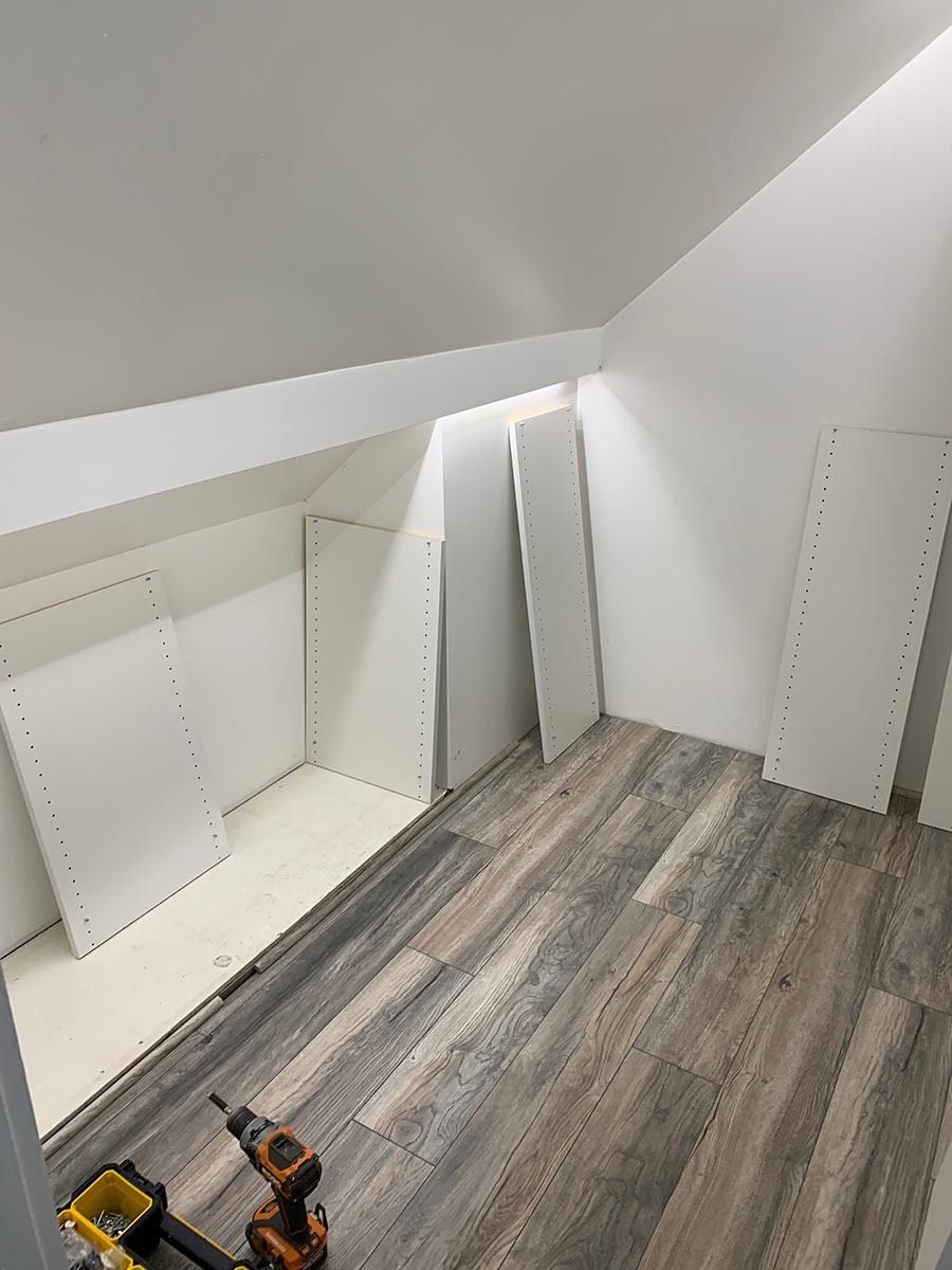 White closet interior with sloped ceiling, wood-look floor, and shelves being assembled.