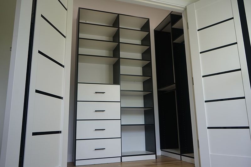 Built-in closet organizer with shelves and drawers, framed by white doors with black accents.