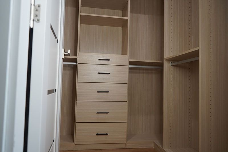 Empty, light-wood closet with shelves, drawers, and hanging rods.  Open doorway on the left.