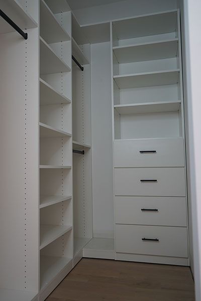 White walk-in closet with shelves, drawers, and hanging rods. Interior is modern with light wood floor.