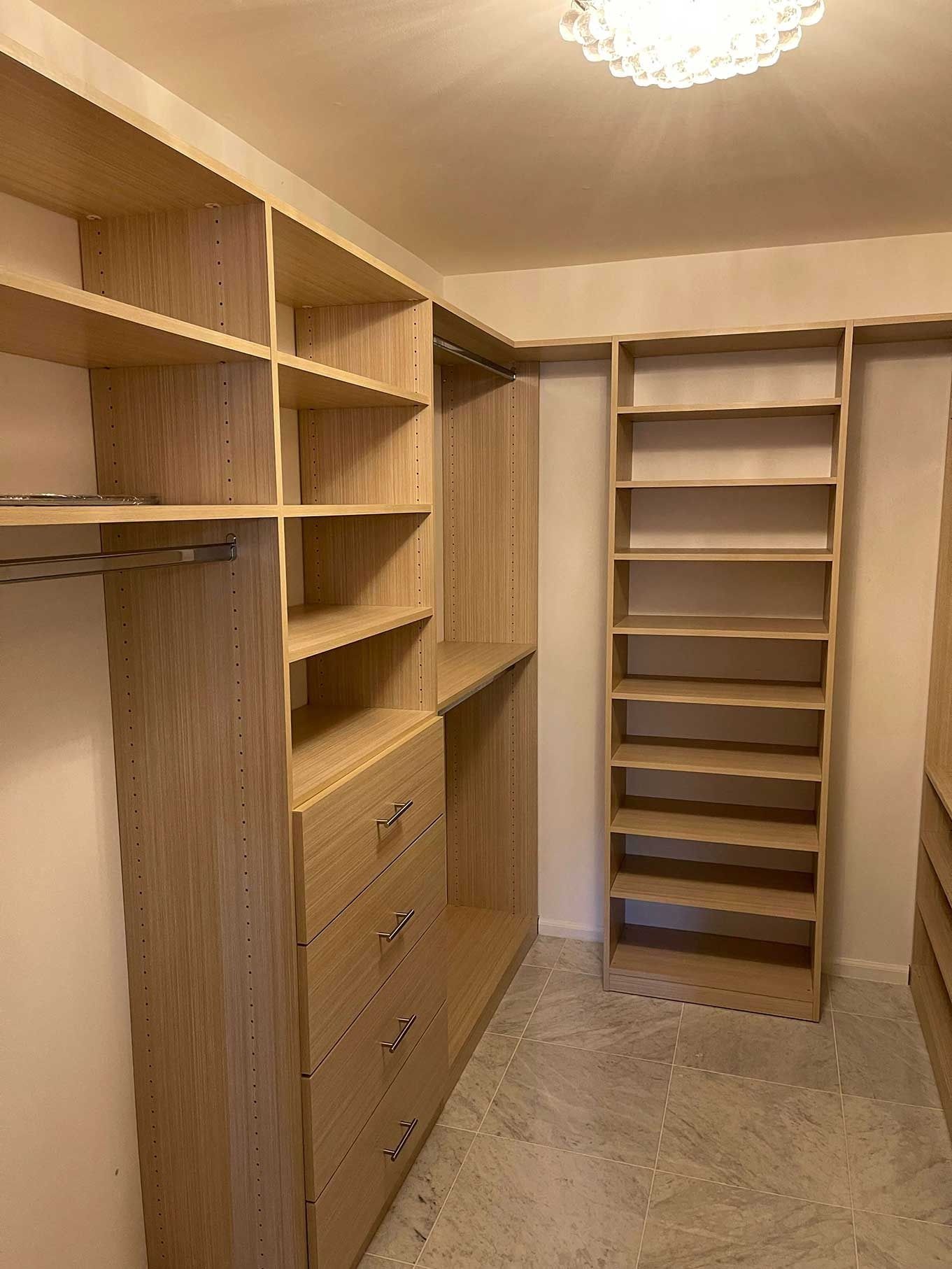 Empty walk-in closet with light wood shelving, drawers, and rod; a neutral, well-lit space.