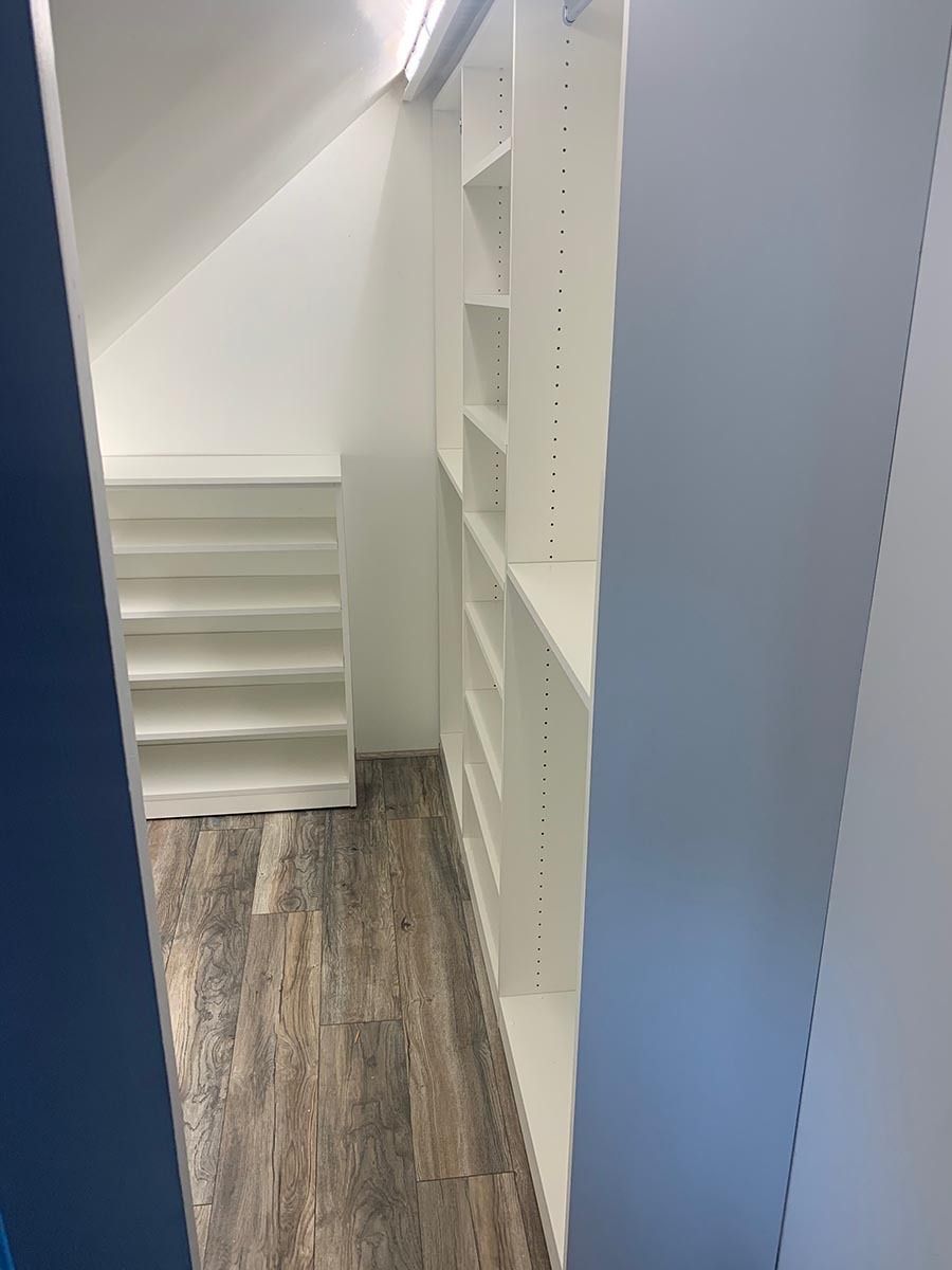 White built-in shelving in a small room with angled ceiling and wood-look flooring.