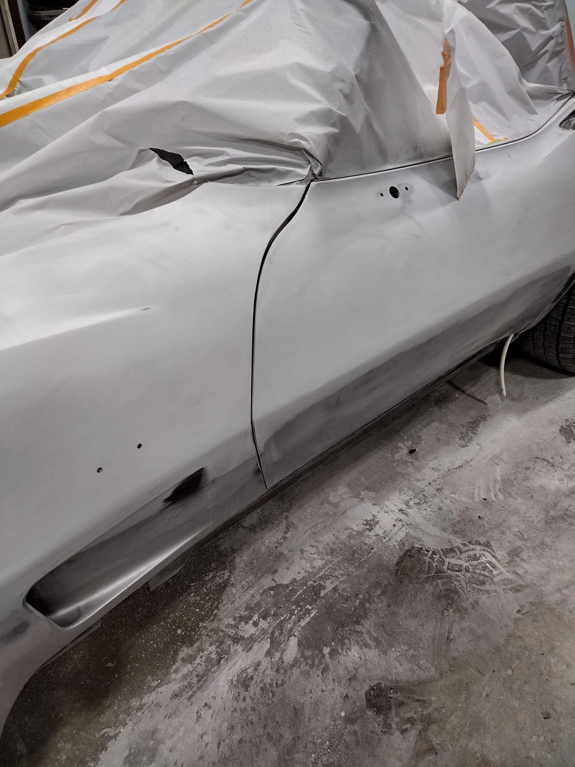 Gray car door with vertical crack, covered in plastic sheeting.
