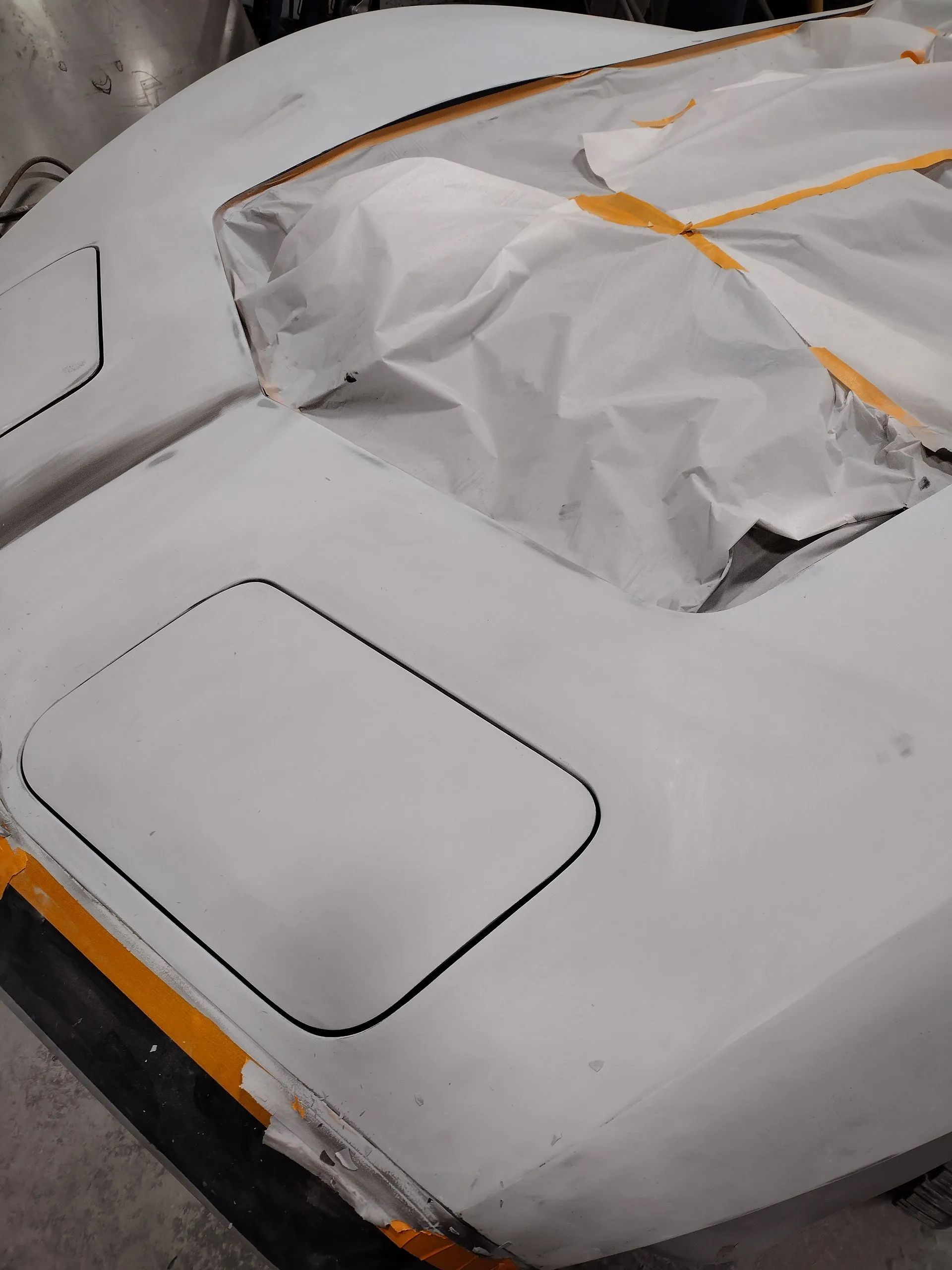 White car hood with taped edges, masked window area, ready for paint.