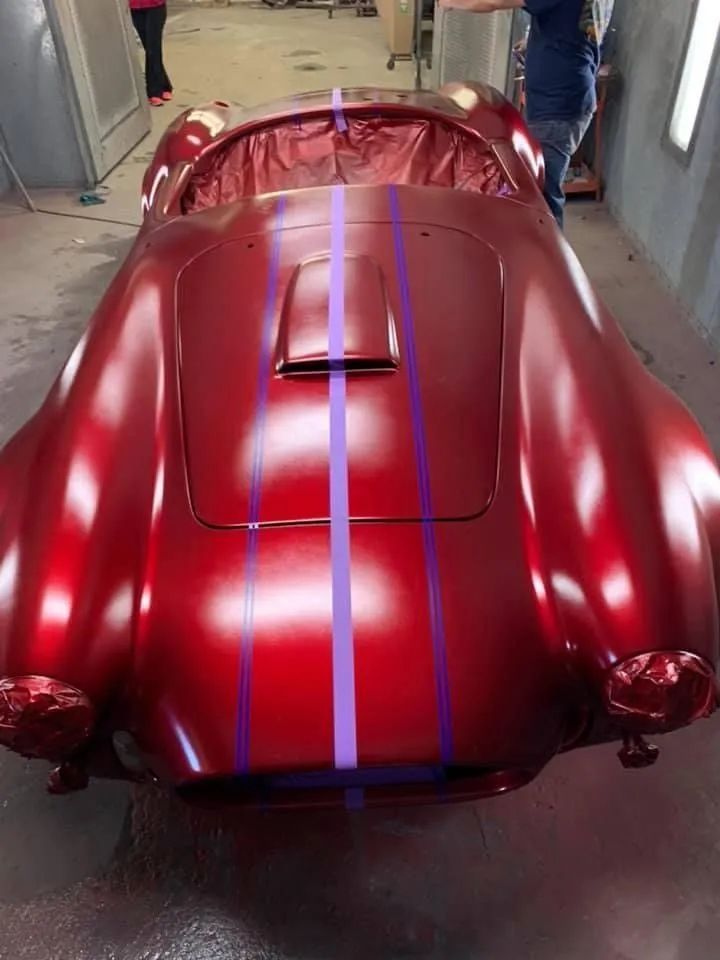 Red classic car with purple stripes, in a workshop.