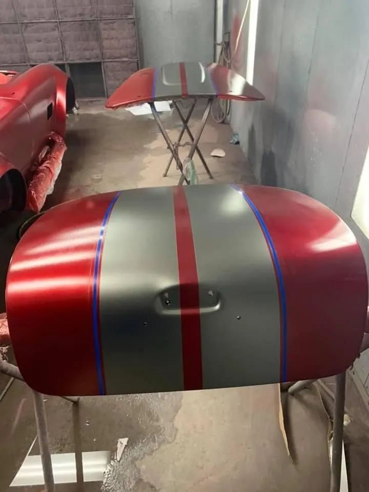 Red car hood with silver stripe and blue outlines, in a paint booth.