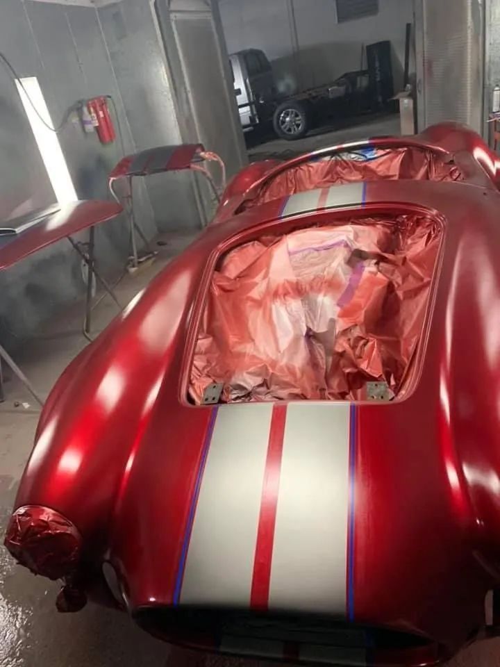 Red sports car being painted with silver and red stripes in a workshop.