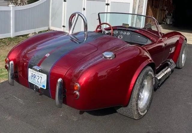 Red Shelby Cobra replica with black stripes, parked outside.