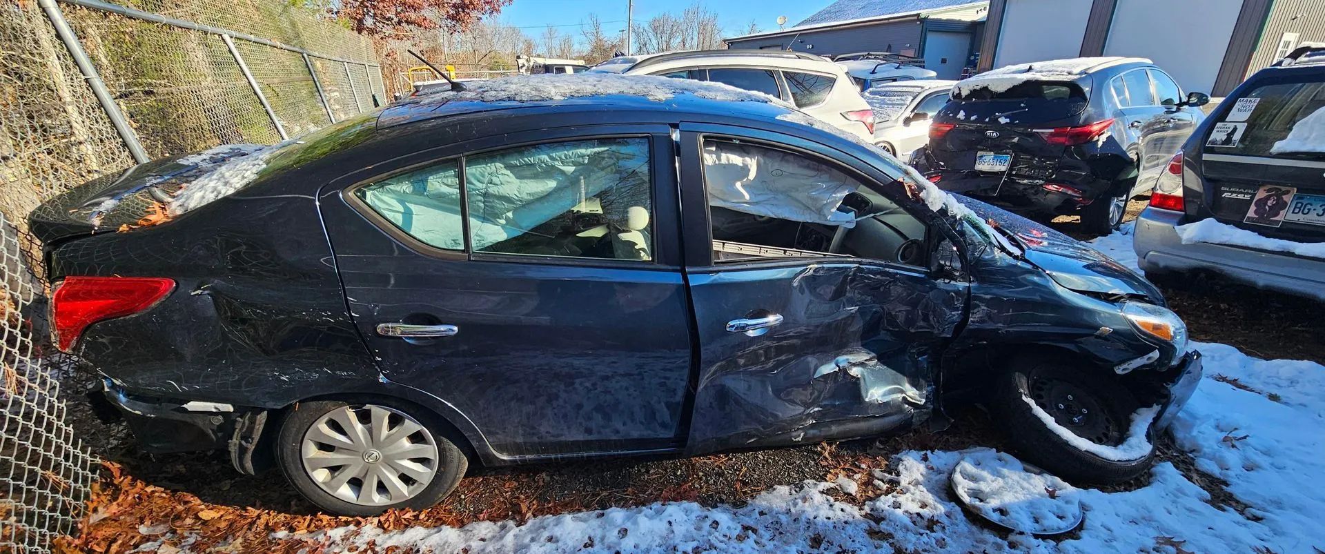 A black sedan heavily damaged in a crash, parked in a snowy area.