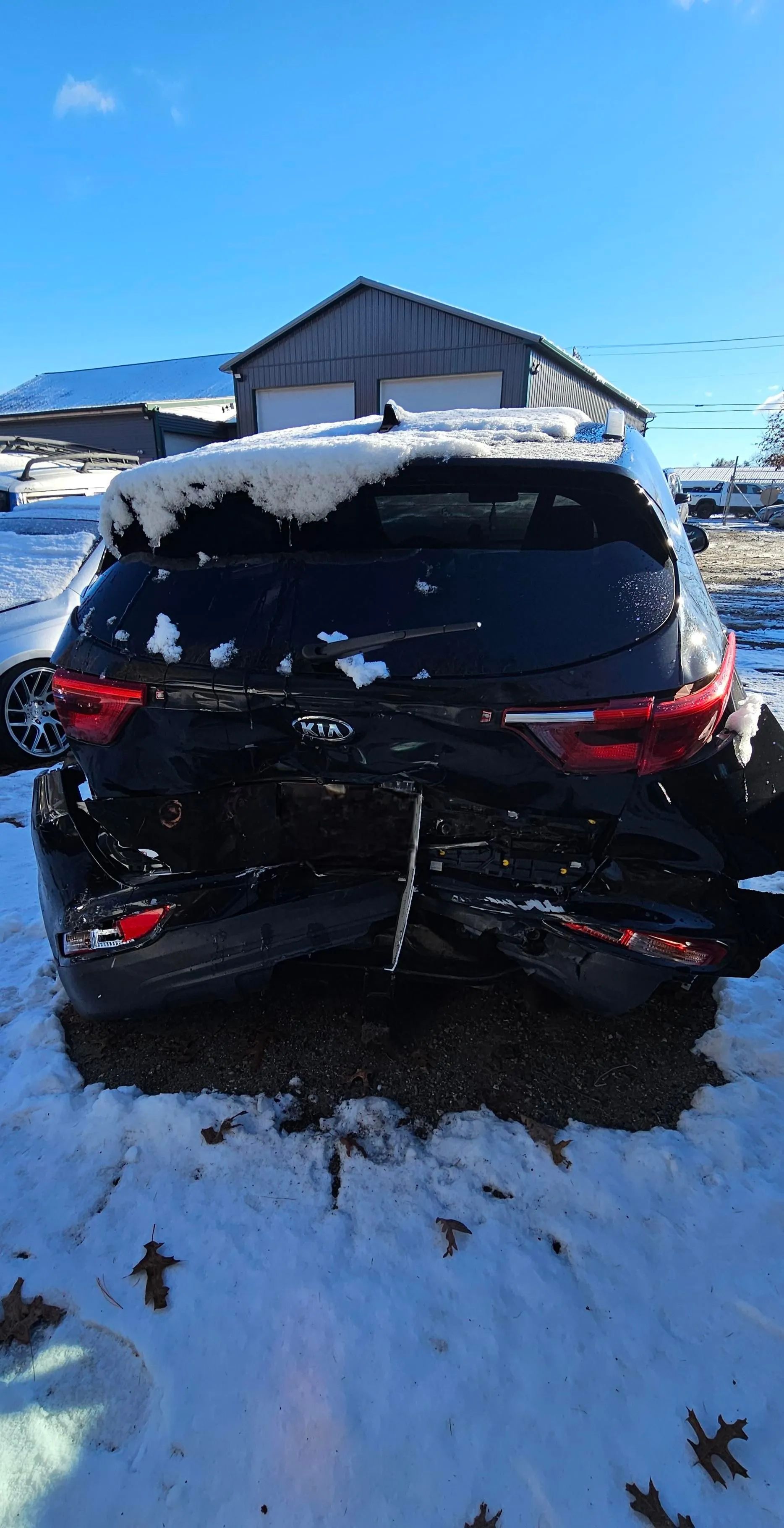 Black SUV with severe rear-end damage, covered in snow, in a snowy outdoor setting.