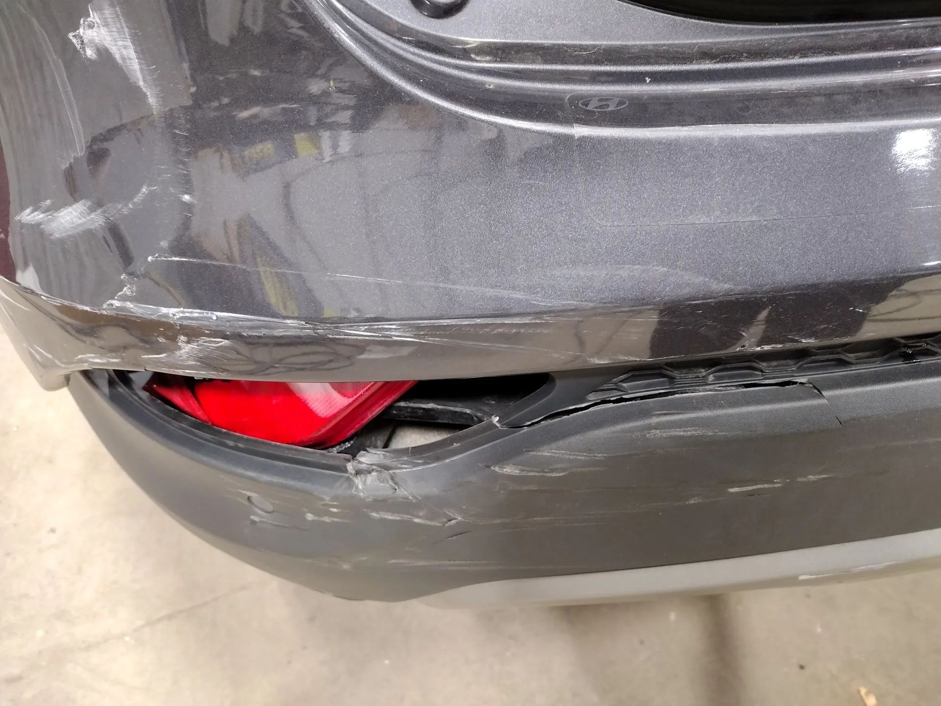 Damaged gray car bumper showing scratches and a red reflector.